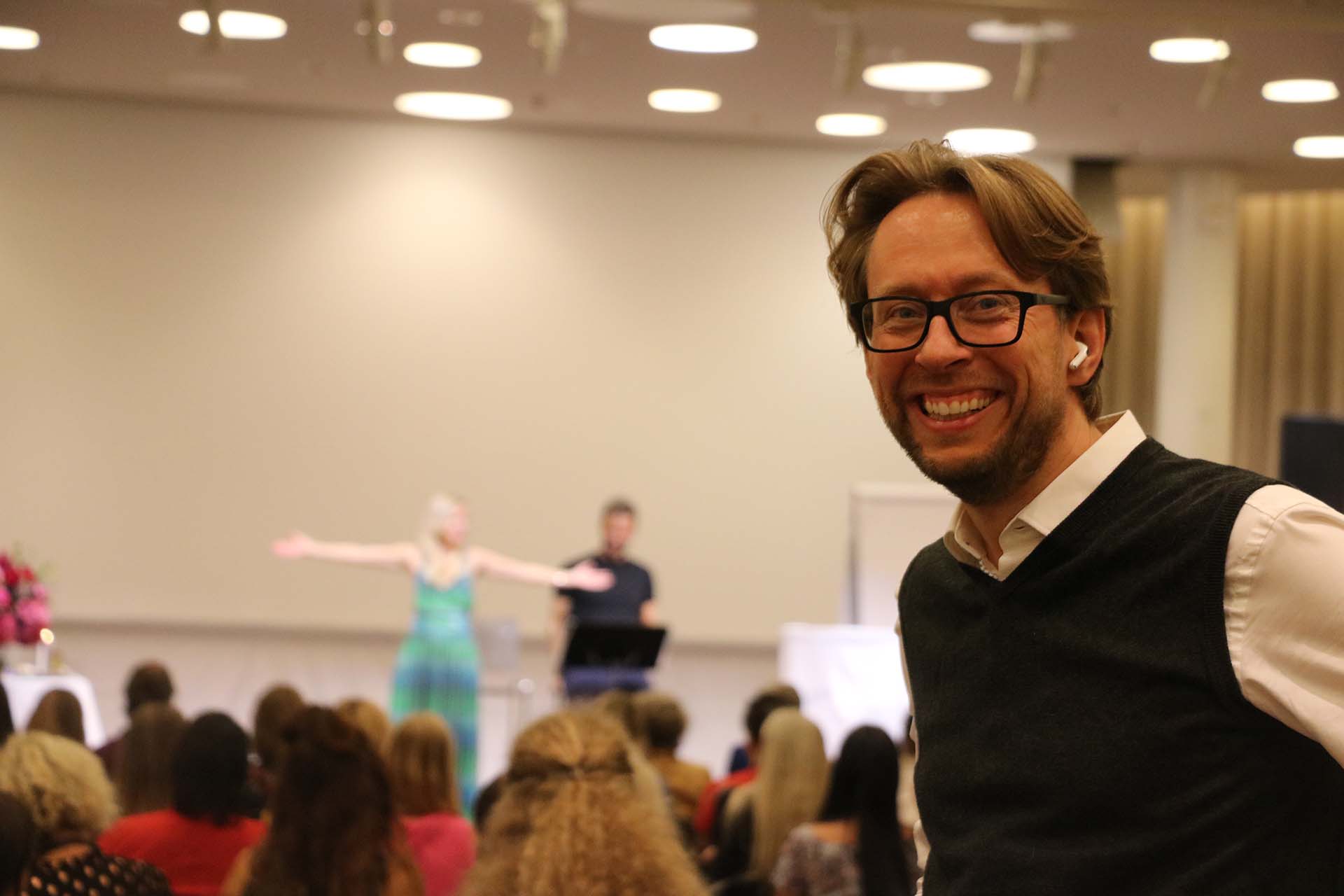 Daniel Schwenger smiling in the audience while speakers perform on stage
